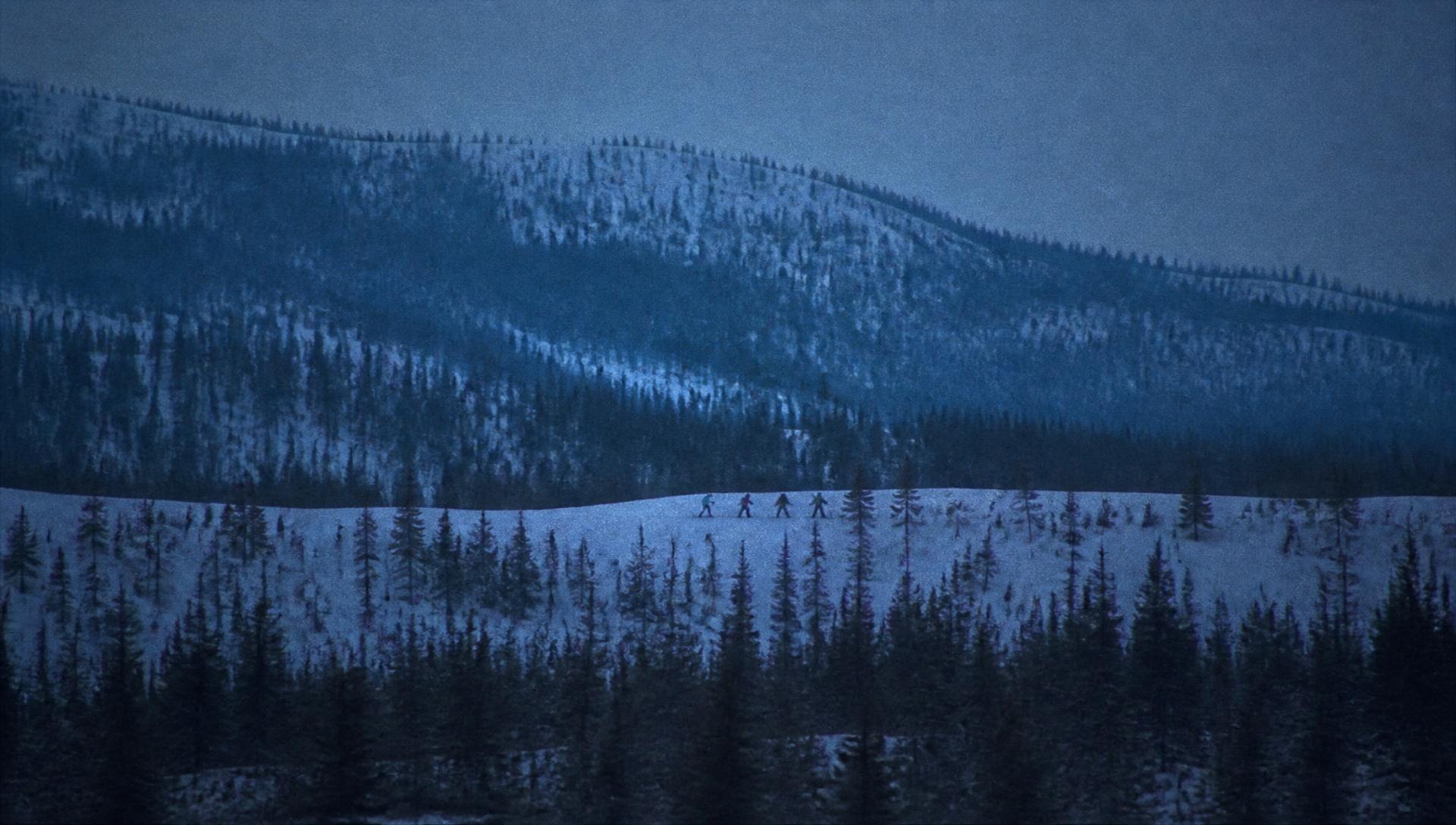 Small group of runners crossing a snowy northern ridge at blue hour